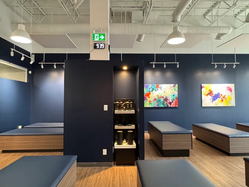 Completed Aurora studio — treatment benches around a blue partition with a display of massage guns and rollers.