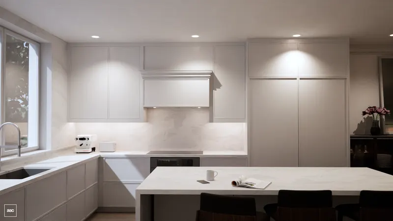 White kitchen cabinetry, pale counters and a long island beside a dark sideboard with flowers.